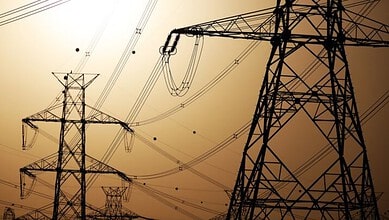 High voltage power lines and towers silhouetted against a sunset sky.
