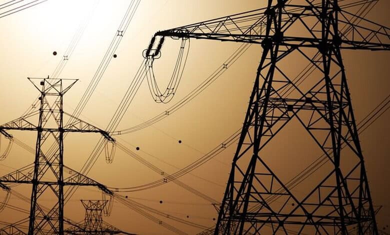 High voltage power lines and towers silhouetted against a sunset sky.