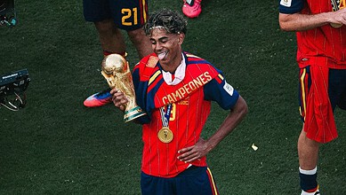 Lamine Yamal celebrating with the World Cup trophy, wearing Spain's red and blue kit.