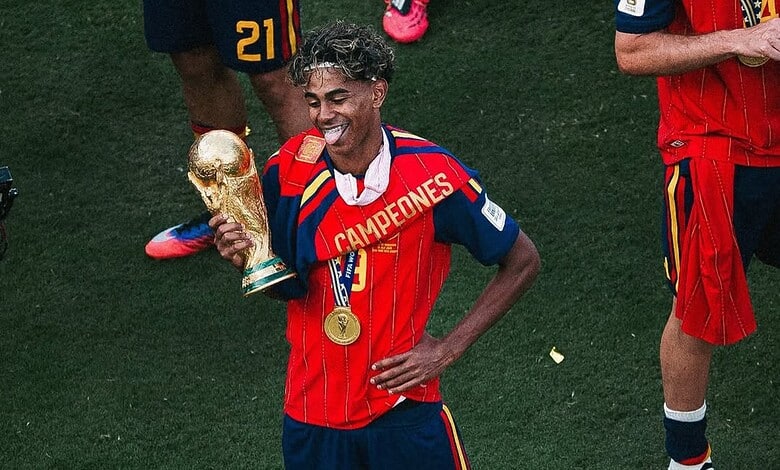 Lamine Yamal celebrating with the World Cup trophy, wearing Spain's red and blue kit.