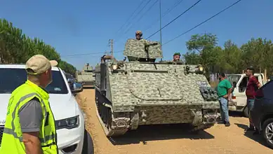A Lebanese army armoured vehicle drives along a road in southern Lebanon as soldiers and civilians stand nearby.