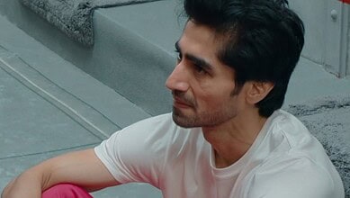 Man with dark hair and stubble in a white T-shirt sitting on stairs.