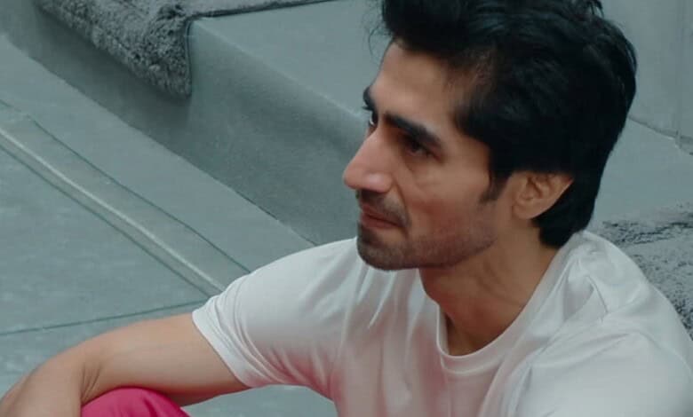 Man with dark hair and stubble in a white T-shirt sitting on stairs.