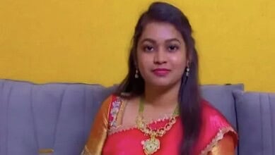 Young woman in traditional attire sitting on a sofa against a yellow wall.