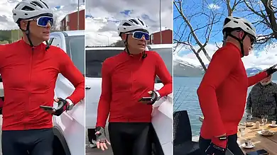 Female cyclist in red jacket and helmet using smartphone outdoors.
