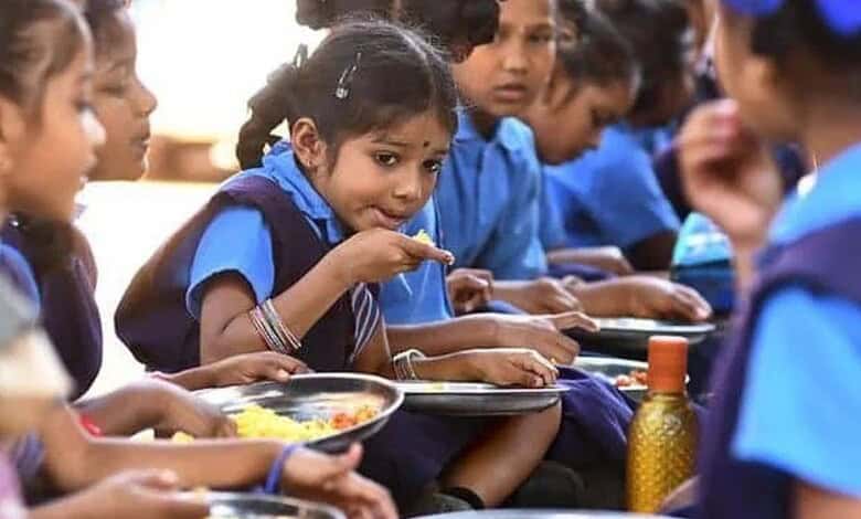 Young schoolgirls in blue uniforms eating a midday meal together, seated in a row with steel plates of rice.