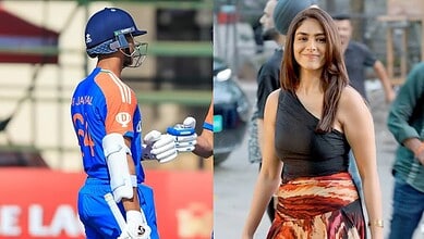 Indian cricketer in blue uniform with helmet and gloves at a cricket ground.