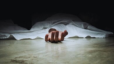 A body covered with a white sheet, with one hand exposed lying on the floor.