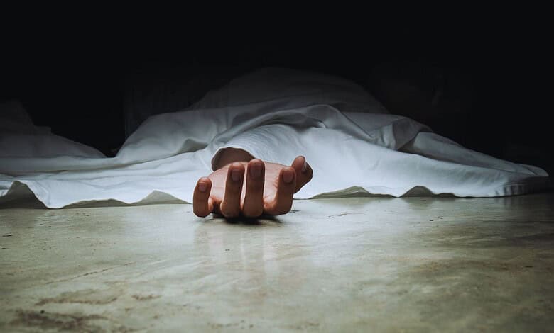 A body covered with a white sheet, with one hand exposed lying on the floor.