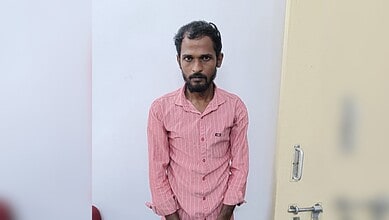 Man in pink shirt standing indoors with a serious expression.