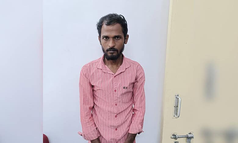 Man in pink shirt standing indoors with a serious expression.