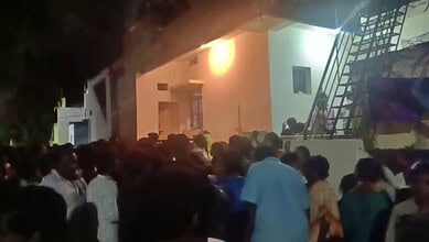Large crowd gathered outside a building during nighttime, some people looking inside or waiting.
