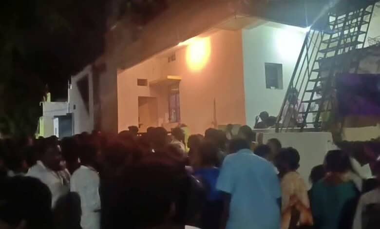 Large crowd gathered outside a building during nighttime, some people looking inside or waiting.