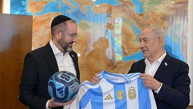 Benjamin Netanyahu and Argentine official holding a football and a jersey in front of a world map.