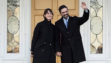 Business professionals shaking hands in a modern office setting, smiling and dressed in formal attire.