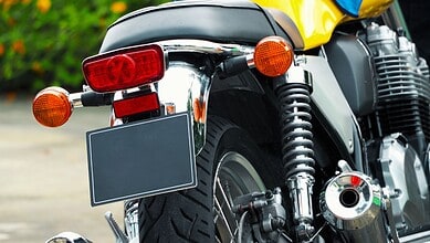 Rear view of a motorcycle with a blank black number plate, chrome fender, and yellow fuel tank visible above