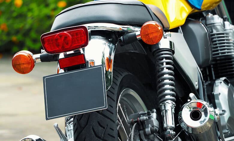 Rear view of a motorcycle with a blank black number plate, chrome fender, and yellow fuel tank visible above