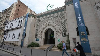 People walking past the historic Paris Grand Mosque with decorative archway and banners marking its cent.
