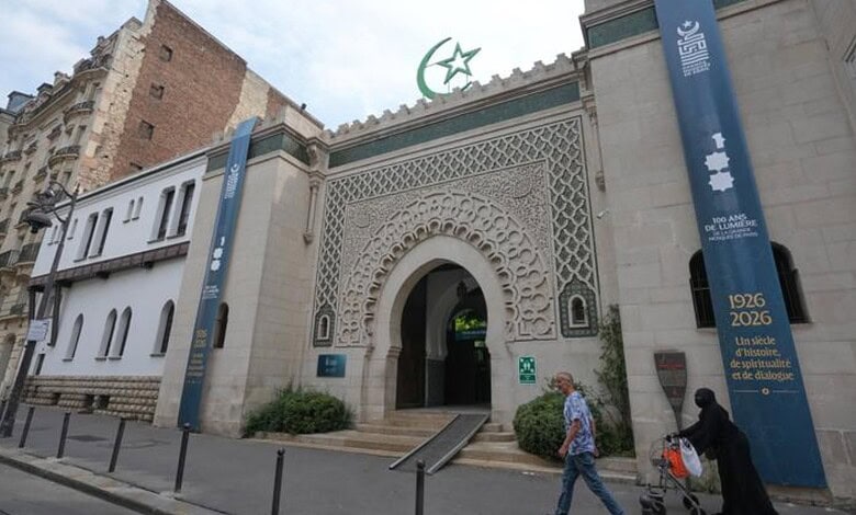 People walking past the historic Paris Grand Mosque with decorative archway and banners marking its cent.