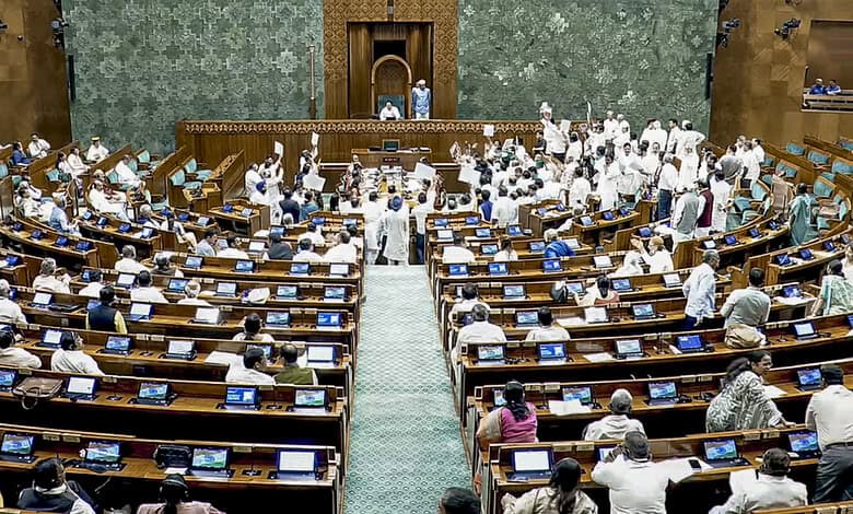 Parliament session with members engaged, some standing, in a large hall with green decor.