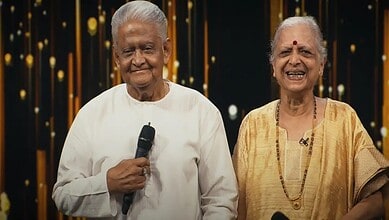 Elderly man and woman smiling at an event, woman holding a shawl, in a festive setting.