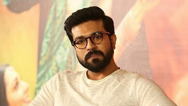 Ram Charan with glasses and beard in a casual setting, looking serious.