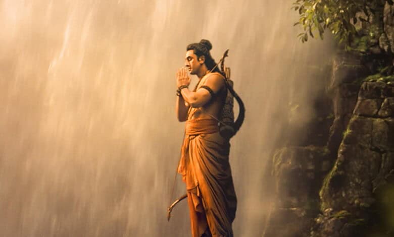 A man dressed as Lord Rama praying near a waterfall in a forest setting.