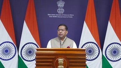 Indian government official speaking at a podium with Indian flags in the background.