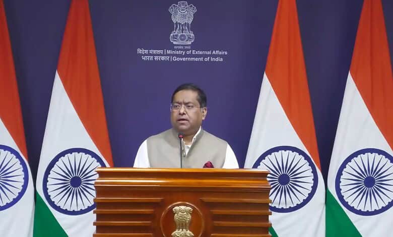 Indian government official speaking at a podium with Indian flags in the background.