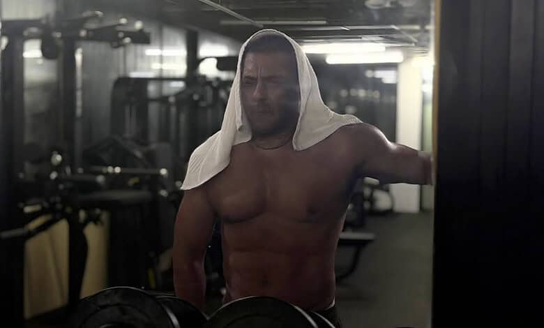 Salman Khan shirtless in gym with a towel on his head, working out intensely.