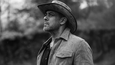 Salman Khan in a black and white photo wearing a hat and casual shirt.
