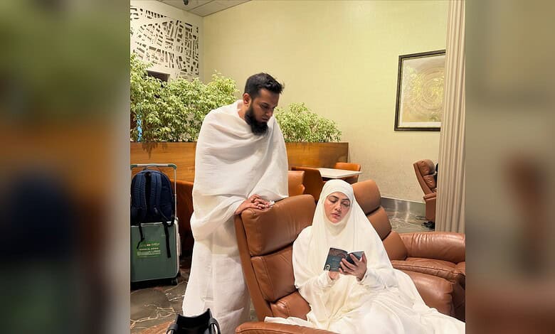 Sana Khan sitting on a brown leather chair, reading a book, with a man standing beside her in a waiting l.