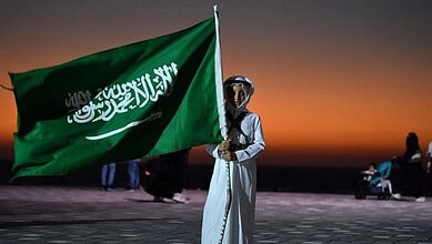 Person holding Saudi Arabia flag during sunset at the beach.