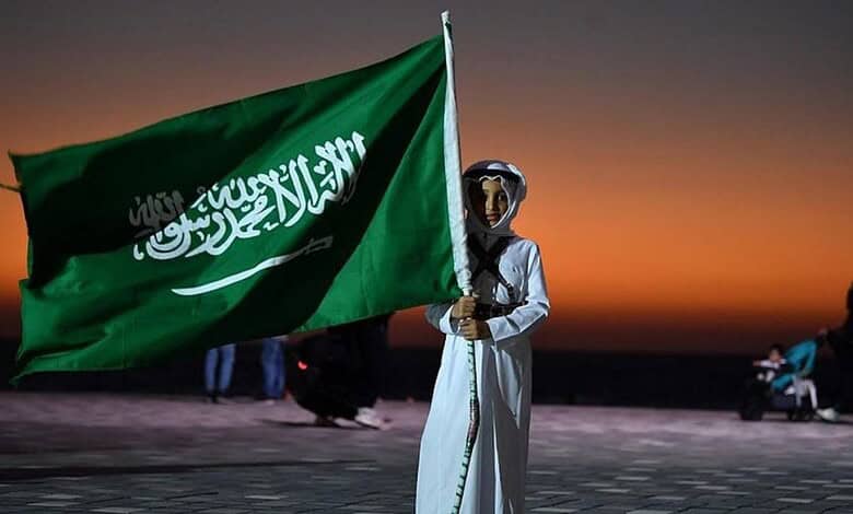 Person holding Saudi Arabia flag during sunset at the beach.