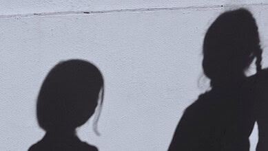 Silhouettes of four school girls against a plain wall, shadowed and indistinct.
