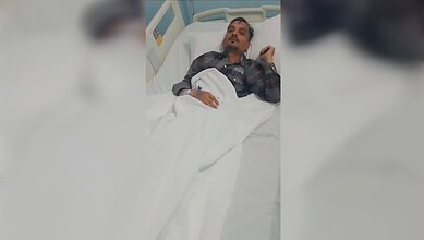 Woman lying in hospital bed, looking distressed, with a bandage on her hand, in a medical setting.