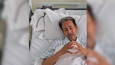 Wangchuk in hospital bed making a heart shape with his hands.