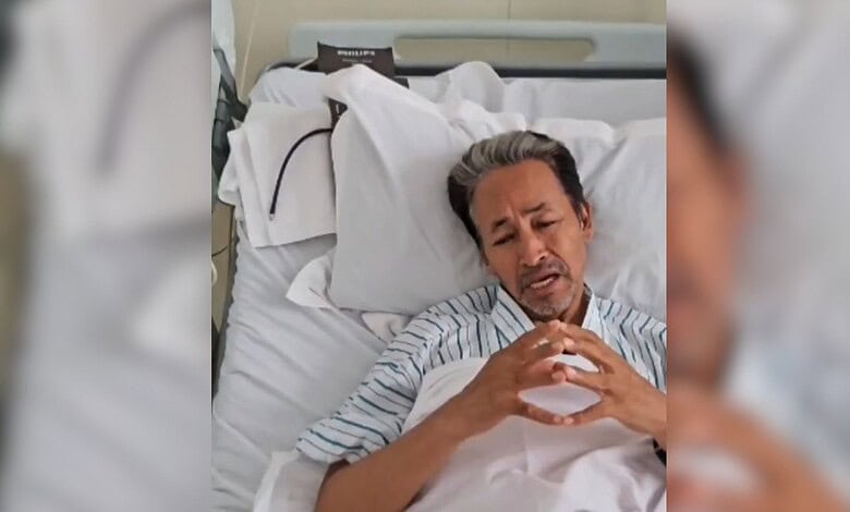 Wangchuk in hospital bed making a heart shape with his hands.