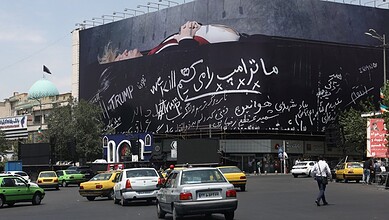 Busy city street with taxis, pedestrians, and large billboards in an urban setting.