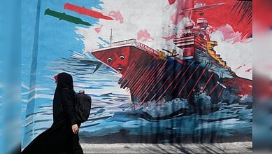 A woman in black walking past a colourful mural of a ship on a city wall.