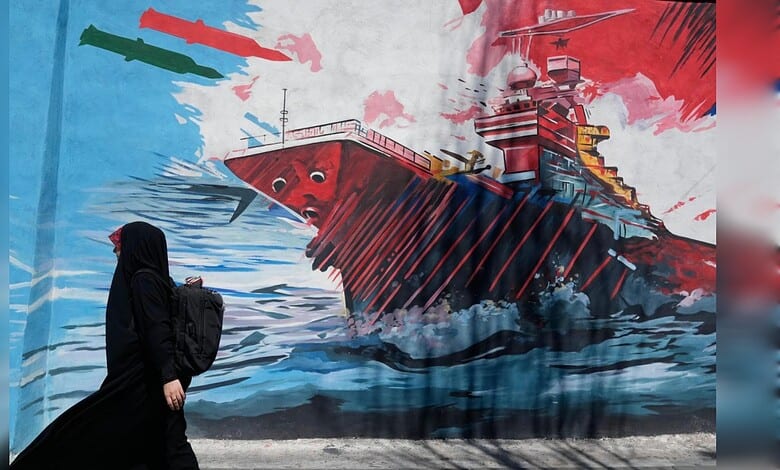 A woman in black walking past a colourful mural of a ship on a city wall.