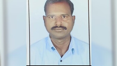 Portrait of a man with mustache wearing a light blue shirt, looking directly at the camera.