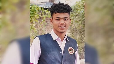 Smiling young man in school uniform with a badge, outdoors in natural light.