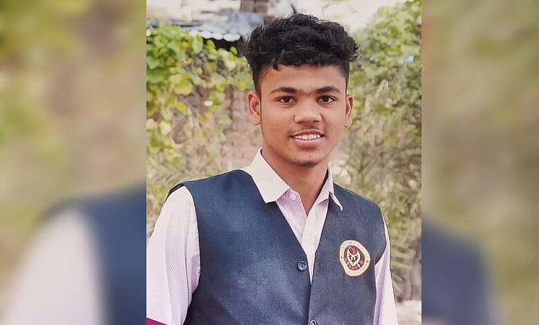 Smiling young man in school uniform with a badge, outdoors in natural light.