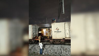 Person climbing on top of a goods train at night, with another person watching below.