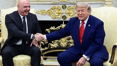 Donald Trump shaking hands with a man in a formal setting, both smiling and seated in ornate chairs.