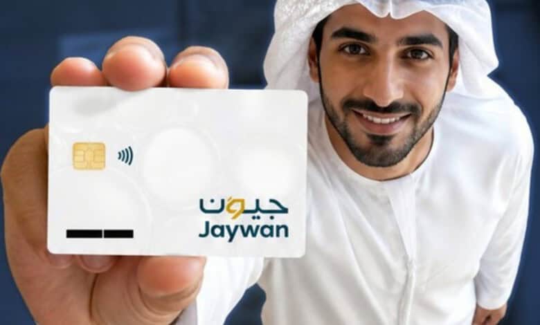 Man holding UAE Jaywan card with contactless payment symbol, smiling at camera.