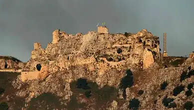 Ruins of an ancient castle on a hilltop with a cloudy sky in the background.