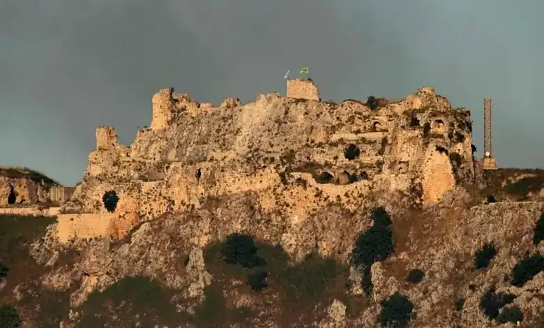 Ruins of an ancient castle on a hilltop with a cloudy sky in the background.