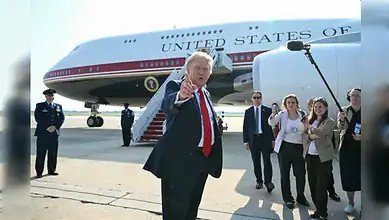 Donald Trump gesturing towards the camera as he disembarks from Air Force One with staff and security.